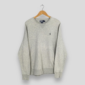 May include: A light gray sweatshirt with a crew neck and long sleeves, hanging from a wooden hanger. A small black logo is embroidered on the left chest. The sweatshirt is made of a soft, comfortable material.