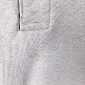 May include: Close-up of a light gray polo shirt collar. The collar features a buttoned placket and is made of a soft, textured fabric. The stitching is visible, and there are some light stains on the fabric.