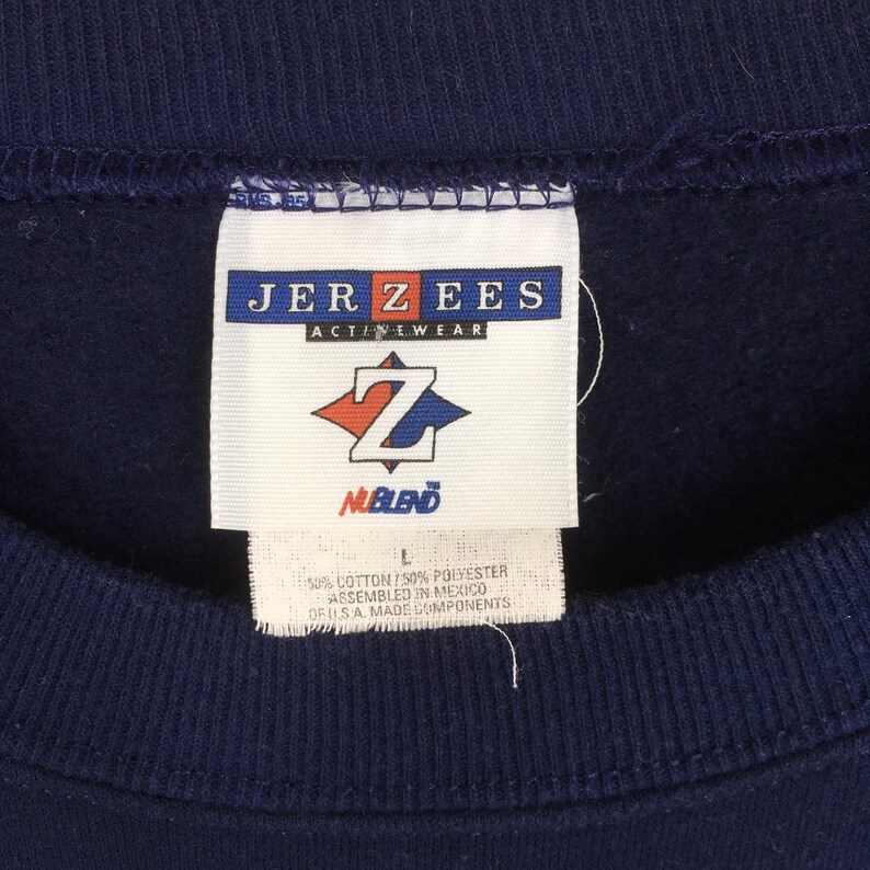 May include: Close-up of a navy blue sweatshirt tag. The tag reads "JERZEES ACTIVEWEAR" with a logo and "NUBLEND" below. The tag also indicates the garment is 50% cotton and 50% polyester, assembled in Mexico.