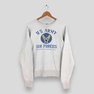 May include: A light gray sweatshirt with the text "U.S. ARMY AIR FORCES" in blue and gold. The design includes a circular emblem with a star and wings. The sweatshirt is hanging on a wooden hanger.