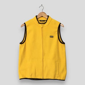 May include: A bright yellow fleece vest featuring a full-length front zipper, a stand-up collar, and black trim along the armholes, hem, and collar. A small black rectangular patch with the white text Polo Ralph Lauren is on the left chest.