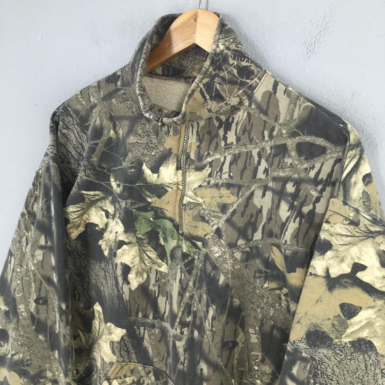 Pode incluir: Um moletom com z&iacute;per com estampa de camuflagem. O moletom apresenta gola alta e fecho de meio z&iacute;per. O design de camuflagem incorpora tons de marrom, verde e bege, imitando um ambiente florestal. A pe&ccedil;a &eacute; feita de um material macio, possivelmente semelhante ao fleece.