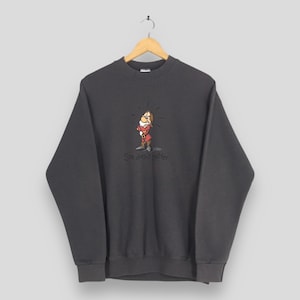 Peut inclure: Sweat-shirt gris foncé avec une illustration de dessin animé d'un nain en tenue rouge. Le texte "She doesn't matter" est imprimé en dessous. Le sweat-shirt est suspendu à un cintre en bois.
