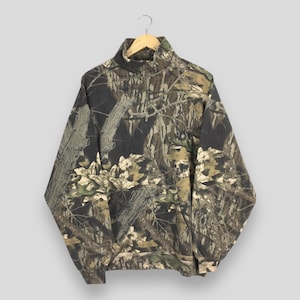 May include: A camouflage-patterned pullover sweatshirt with a half-zip closure. The design features a mix of brown, green, and tan hues, mimicking a forest environment. The sweatshirt has a high collar and long sleeves, suitable for outdoor activities.