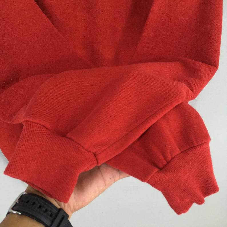 Peut inclure: Gros plan sur une manche de sweat-shirt rouge. La manche est faite d'un tissu doux et textur&eacute; et poss&egrave;de un poignet c&ocirc;tel&eacute;. Une montre est visible au poignet.