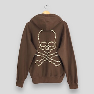 May include: Brown hooded sweatshirt with a skull and crossbones design made of white studs on the back.
