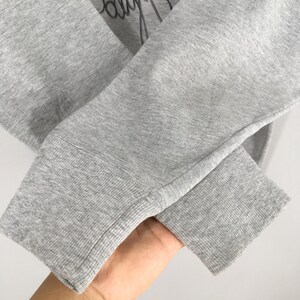 May include: Close-up of a gray sweatshirt sleeve with a ribbed cuff. The fabric is a heathered gray, and the cuff is a darker shade of gray. The sleeve is slightly wrinkled.