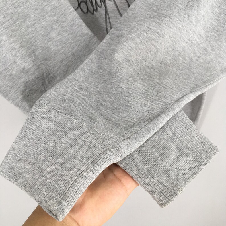 May include: Close-up of a gray sweatshirt sleeve with a ribbed cuff. The fabric is a heathered gray, and the cuff is a darker shade of gray. The sleeve is slightly wrinkled.