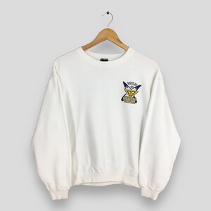 Op de afbeelding: Een witte crewneck sweatshirt met een grafische print op de voorkant. De afbeelding heeft een geel en paars ontwerp met de tekst "BOYS LIFE" en "GOLDEN GATE" in een rechthoekige doos.