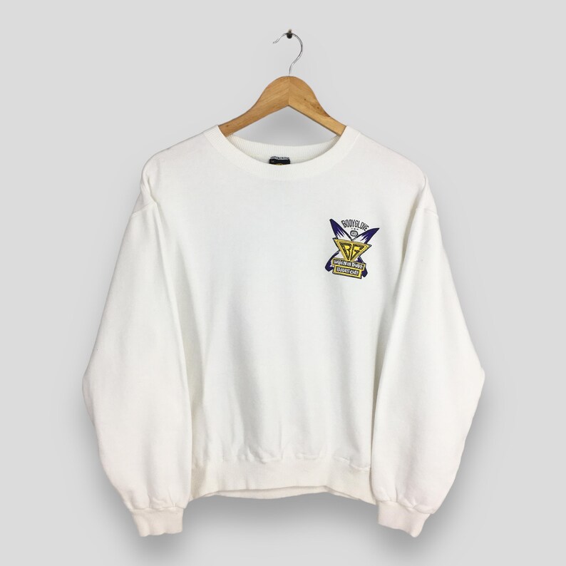 Op de afbeelding: Een witte crewneck sweatshirt met een grafische print op de voorkant. De afbeelding heeft een geel en paars ontwerp met de tekst "BOYS LIFE" en "GOLDEN GATE" in een rechthoekige doos.
