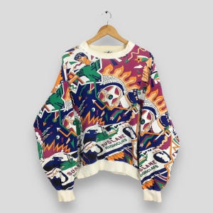 May include: A vintage crew neck sweatshirt with a vibrant, all-over print. The design features a mix of geometric shapes, flames, and figures in shades of blue, purple, green, and orange. The cuffs and collar are cream-colored, and the text "SUSLANE HIGHCLASS" is visible.