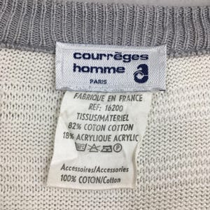 May include: Close-up of a white and gray knit sweater with a label. The label reads "courr&egrave;ges homme PARIS" and includes fabric composition details: 82% cotton, 18% acrylic. The sweater's collar is gray.