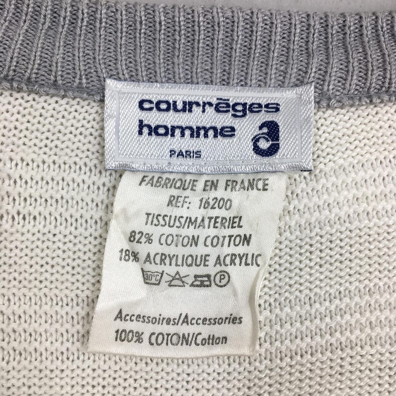 May include: Close-up of a white and gray knit sweater with a label. The label reads "courr&egrave;ges homme PARIS" and includes fabric composition details: 82% cotton, 18% acrylic. The sweater's collar is gray.