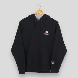 May include: Black hooded sweatshirt with a kangaroo pocket and drawstring. The sweatshirt features a small red and white logo on the chest and a smaller logo on the left sleeve. The brand name "eckō unltd." is printed on the chest.