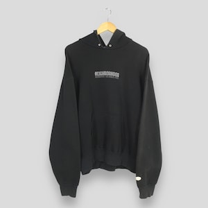 May include: Black hooded sweatshirt with the word "NEIGHBORHOOD" printed across the chest. The sweatshirt has a kangaroo pocket and ribbed cuffs and hem. The garment is hanging on a wooden hanger.