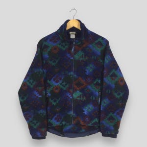 May include: A navy blue fleece jacket with a full zipper and a high collar. The jacket features a geometric pattern in shades of blue, green, and maroon. It has two side pockets and a small logo on the chest.
