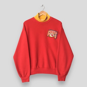 Peut inclure: Un sweat-shirt rouge &agrave; manches longues avec un col montant jaune et un &eacute;cusson Kansas City Chiefs sur la poitrine droite. Le logo affiche le mot CHIEFS en lettres jaunes et rouges accompagn&eacute; d'un embl&egrave;me en forme de pointe de fl&egrave;che.
