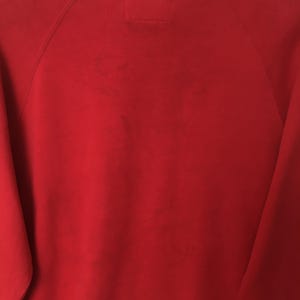 Op de afbeelding: Een effen rood sweatshirt met lange mouwen, raglanmouwen en een zichtbare stiknaad in het midden van de halslijn. De stof heeft een gladde, uniforme textuur met subtiele variaties in de rode kleur over het gehele oppervlak.