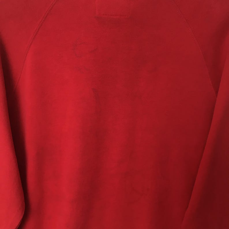 Op de afbeelding: Een effen rood sweatshirt met lange mouwen, raglanmouwen en een zichtbare stiknaad in het midden van de halslijn. De stof heeft een gladde, uniforme textuur met subtiele variaties in de rode kleur over het gehele oppervlak.