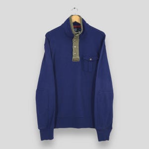 May include: A navy blue sweatshirt with a high collar and olive green accents. The sweatshirt features a button-up closure, a small pocket, and elbow patches. The Polo Ralph Lauren logo is visible on the collar.