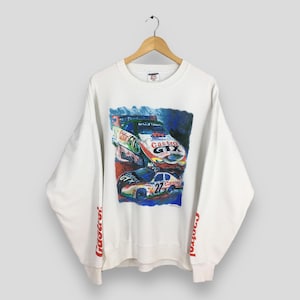 Puede incluir: Sudadera blanca con un estampado gráfico colorido de coches de carreras. El estampado presenta las palabras "Castrol GTX" y "Castrol" en los coches. Las mangas tienen la palabra "Castrol" impresa en rojo en los puños.