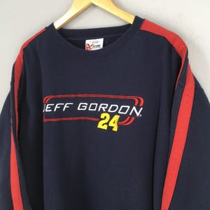 Puede incluir: Sudadera azul marino con detalles en rojo y el texto "JEFF GORDON 24" en rojo y amarillo. La sudadera tiene rayas rojas en las mangas y una etiqueta Chase Authentics.
