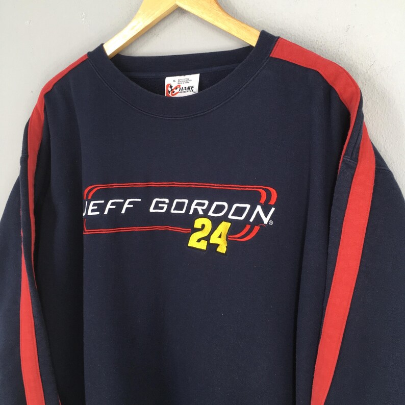 Puede incluir: Sudadera azul marino con detalles en rojo y el texto "JEFF GORDON 24" en rojo y amarillo. La sudadera tiene rayas rojas en las mangas y una etiqueta Chase Authentics.