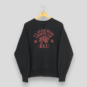 May include: Black crew neck sweatshirt with red graphic text and design. The text reads "U.S. AIR BASE MC RACE A WINNING TEAM" with the numbers "55" and "56" on either side of a motorcycle graphic. The text "D.S.F." is below the graphic.
