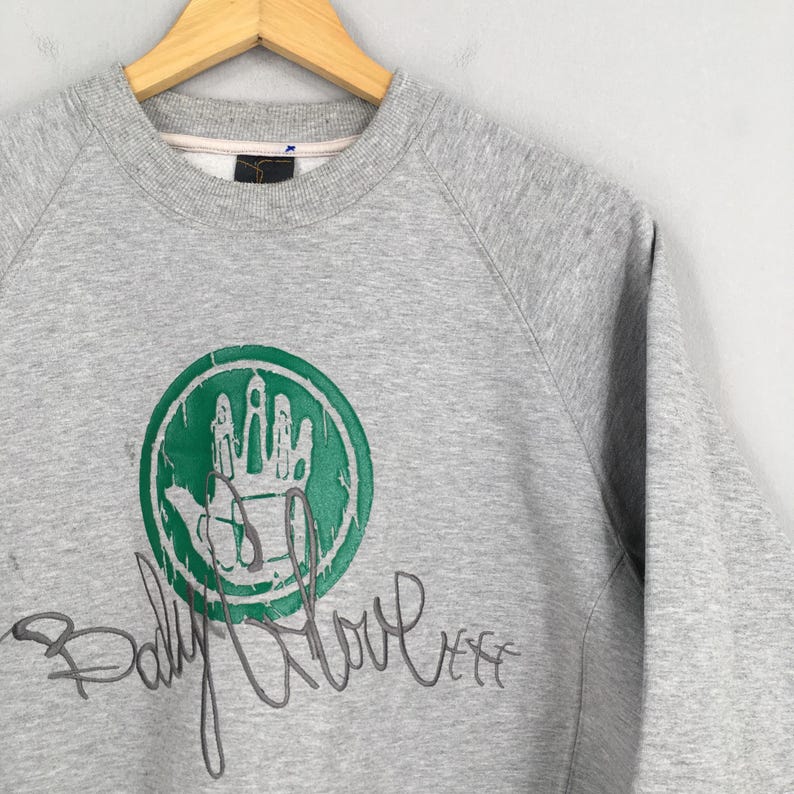 May include: A gray sweatshirt with a green and white circular graphic featuring a hand design. The words "Body Glove" are written in a cursive font below the graphic. The sweatshirt is hanging on a wooden hanger.