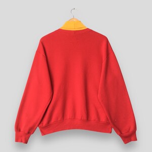 Peut inclure: Un sweat-shirt rouge vif &agrave; manches longues avec un design uni et un col montant jaune moutarde contrastant. Le v&ecirc;tement pr&eacute;sente des manches longues avec des poignets c&ocirc;tel&eacute;s et un ourlet c&ocirc;tel&eacute;, pr&eacute;sent&eacute; sur un cintre en bois simple.
