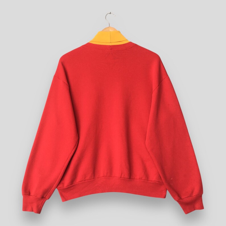 Peut inclure: Un sweat-shirt rouge vif &agrave; manches longues avec un design uni et un col montant jaune moutarde contrastant. Le v&ecirc;tement pr&eacute;sente des manches longues avec des poignets c&ocirc;tel&eacute;s et un ourlet c&ocirc;tel&eacute;, pr&eacute;sent&eacute; sur un cintre en bois simple.