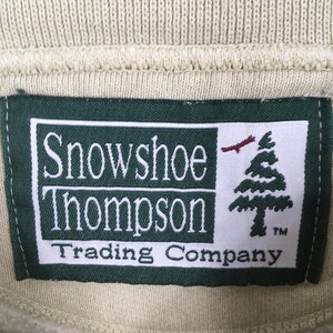 Peut inclure: &Eacute;tiquette verte avec du texte blanc qui dit "Snowshoe Thompson Trading Company" avec un pin stylis&eacute; et un oiseau rouge. L'&eacute;tiquette a une bordure blanche et un fond blanc.