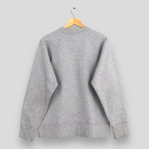 May include: A heather gray sweatshirt hangs from a wooden hanger. The crew neck sweatshirt has long sleeves with ribbed cuffs. The back of the sweatshirt is visible, showing the raglan sleeves and the overall shape of the garment.
