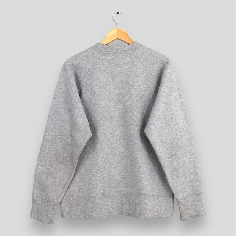 May include: A heather gray sweatshirt hangs from a wooden hanger. The crew neck sweatshirt has long sleeves with ribbed cuffs. The back of the sweatshirt is visible, showing the raglan sleeves and the overall shape of the garment.
