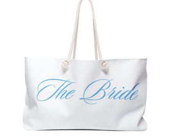 May include: White tote bag with light blue script text that reads "The Bride." The bag has white rope handles and gold-colored hardware. A large, casual bag for carrying items.