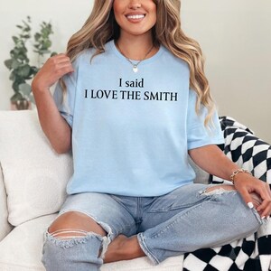 May include: A light blue t-shirt with the text "I said I LOVE THE SMITH" printed in black.