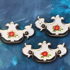 May include: Three white porcelain drawer pulls with ornate floral designs and brass hardware. Each pull features a red rose with green leaves.