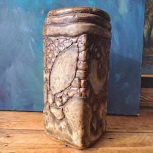 May include: A trio of cream-glazed ceramic mugs, each adorned with a hand-painted floral pattern in blue, green, and yellow. The mugs have a speckled finish and a classic, rounded design with a handle. Ideal for tea or coffee.