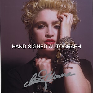 Peut inclure: Portrait d'une personne aux cheveux blonds bouclés, au rouge à lèvres rouge et portant plusieurs bracelets. L'image comprend le texte "HAND SIGNED AUTOGRAPH" et une signature. La personne porte un haut noir.