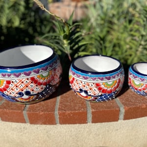 May include: Three hand-painted ceramic bowls with a vibrant floral design. The bowls feature a white interior, a blue rim, and colorful patterns in red, orange, yellow, and blue. The bowls are of varying sizes, perfect for decorative use.