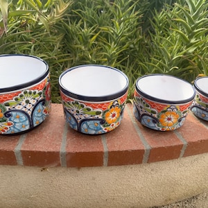 May include: A set of four graduated ceramic bowls featuring a vibrant hand-painted floral pattern in orange, blue, green, and yellow. Each bowl has a white interior and a dark blue rim, showcasing intricate decorative motifs on the exterior surface.