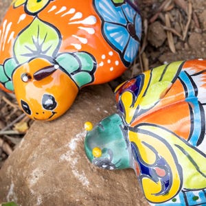 May include: Two colorful ceramic turtle figurines with intricate floral designs painted in shades of orange, yellow, green, blue, and white.