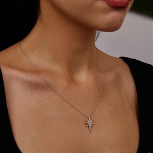 May include: A silver chain necklace with a star-shaped pendant encrusted with small clear stones. The pendant is a pointed star with a long, thin point.