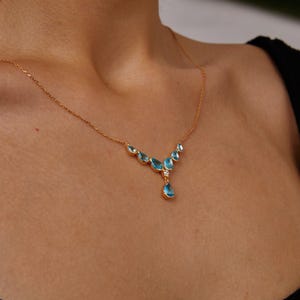 May include: A gold necklace with a teardrop-shaped pendant and smaller teardrop-shaped stones in a V-shape.
