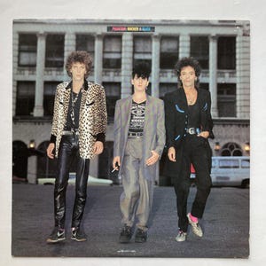 May include: Album cover featuring three men in 1980s attire. The man on the left wears a leopard print jacket and leather pants. The man in the middle wears a gray suit and the man on the right wears a black suit. The album title "Phantom, Rocker & Slick" is at the top.