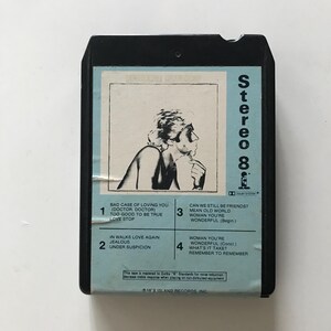 May include: A black cassette tape with a blue label. The label features a black and white photo of a person with short hair. The text on the label reads "Stereo 8" and lists the song titles "Bad Case of Loving You (Doctor, Doctor)", "Too Good to Be True", "Love Stop", "Can We Still Be Friends?", "Mean Old World", "Woman You're Wonderful (Begin.)", "In Walks Love Again", "Jealous", "Under Suspicion", "Woman You're Wonderful (Conc.)", "What's It Take?", and "Remember to Remember". The text at the bottom of the label reads "This tape is mastered to Dolby "B" Standards for noise reduction. Decrease treble response when playing on non-dolbyized equipment. ℗ 1979 ISLAND RECORDS, INC."