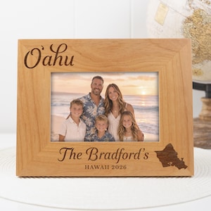 Puede incluir: Un marco de fotos de madera con un retrato familiar. El marco está grabado con "Oahu" en la parte superior y "The Bradford's HAWAII 2026" en la parte inferior, junto con un contorno de la isla hawaiana. Un globo terráqueo está en el fondo.