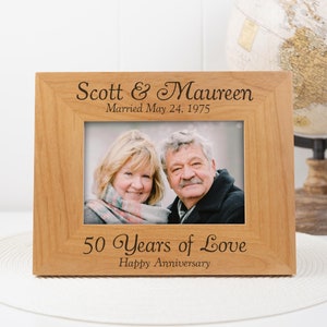 Puede incluir: Un marco de fotos de madera con una foto de una pareja. El marco está grabado con el texto "Scott & Maureen Casados el 24 de mayo de 1975" y "50 años de amor Feliz aniversario".