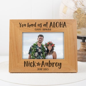 Puede incluir: Un marco de fotos de madera con el texto "You had us at Aloha, Oahu, Hawaii" y "Nick & Aubrey, June 2025". El marco tiene una foto de una pareja en el centro.