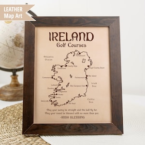 May include: A brown leather map of Ireland with the text "IRELAND Golf Courses" and a list of golf courses throughout the country. The map is framed in a dark brown wood frame. The text "May your swing be straight and the ball fly far. May your round be blessed with no more than par. -IRISH BLESSING" is printed below the map.